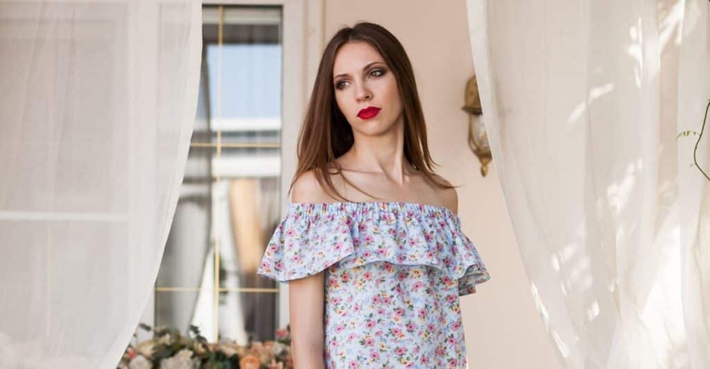 A woman in a white floral off-the-shoulder dress, dark long hair, and red lipstick posing for a photo with a thoughtful, serious face. This photo represents the title of the article, "Identifying and Understanding Covert Narcissistic Women