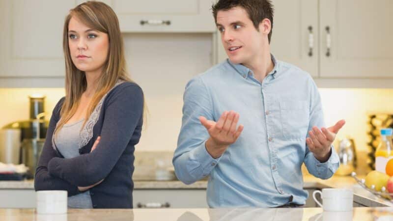 A 20-something couple at a kitchen counter with the woman facing away with her arms crossed and a sad face and the man, with body turned away but facing her with his hands held up in front of him as if to say, "What, I don't get why you're reacting this way." This picture represents the article, "Help! My Husband is a Covert Narcissist!"