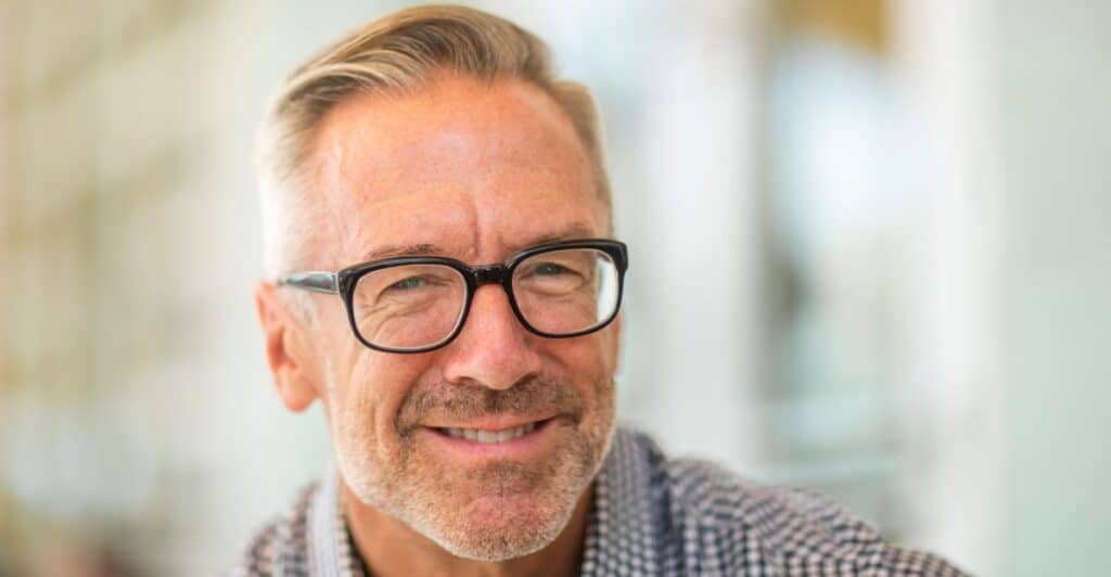 A handsome older man with glasses and a charming smile, depicting the title of the article, "Defending Yourself Against the Aging Narcissist."