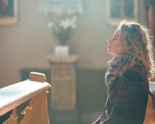 A woman sitting in a church pew, looking up to God in prayer, representing the title of the article, "Working Through the Biblical Consequences of Divorce."