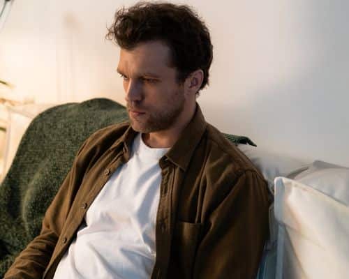 A man sitting back on a couch in a semi-dark room, looking sad. This represents the title of the article, "The Narcissist Reaction to Divorce."