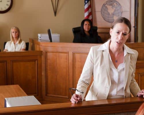 A woman lawyer in court making her argument with a jury member seated and listening behind her. This represents the title of the article, "How to Prove Narcissistic Abuse in Court."