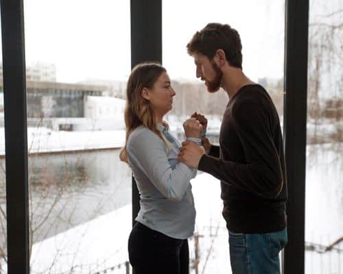 A young man and woman standing very close to each other and facing each other. The man is angry and holding the woman's wrists tightly. The woman looks fearful. This represents the title of the article, "Narcissists Destroy Who They Can't Control."