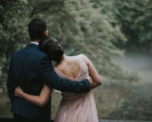 A couple in a forest clearing, dressed in beautiful clothes (man in suit, woman in flowing light pink dress), arm in arm with her head on his shoulder. This article represents when people choose to love each other and stay married. The name of the article is "When is Divorce Okay in the Bible."