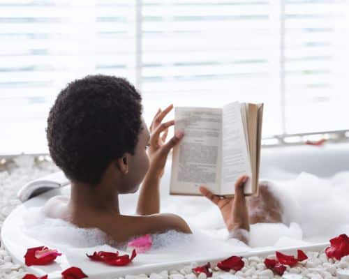 A beautiful woman in a bubble bath with rose petals, reading a book and relaxing for self-care. This photo represents the title of the article, "Surviving a Narcissist: It's Easier Than You Think."