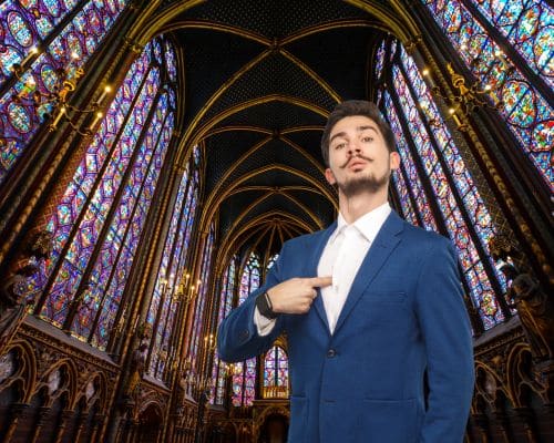 A man in a blue suit in a cathedral with stained glass windows behind him. He is looking very conceited and pointing to himself. This photo represents the title of the article, "What Words Does the Bible Use for Narcissists and Narcissism?"